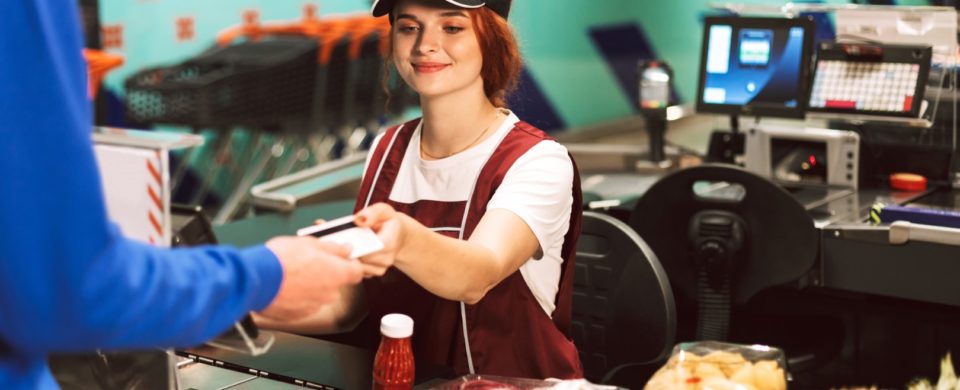 Pretty smiling female cashier in uniform happily working in modern supermarket